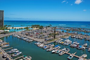 A marina with numerous boats docked, a beach with palm trees, and a clear blue sky. - Ocean-marina Yacht Views Condo Steps to the Beach W/full Kitchen & Free Wifi (Honolulu)