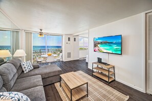 Una sala de estar moderna con un televisor grande, un sofá gris y vistas al océano.