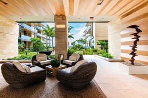 Eine moderne Lobby mit Korbmöbeln, einem zentralen Couchtisch und Blick auf die umliegende Natur und Gebäude.