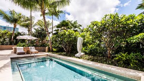 Ein Swimmingpool mit Liegestühlen und einer Statue, umgeben von üppiger Bepflanzung.