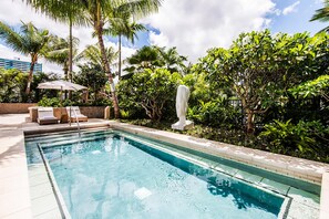 Ein Swimmingpool mit Liegestühlen und einer Statue, umgeben von üppiger Bepflanzung.