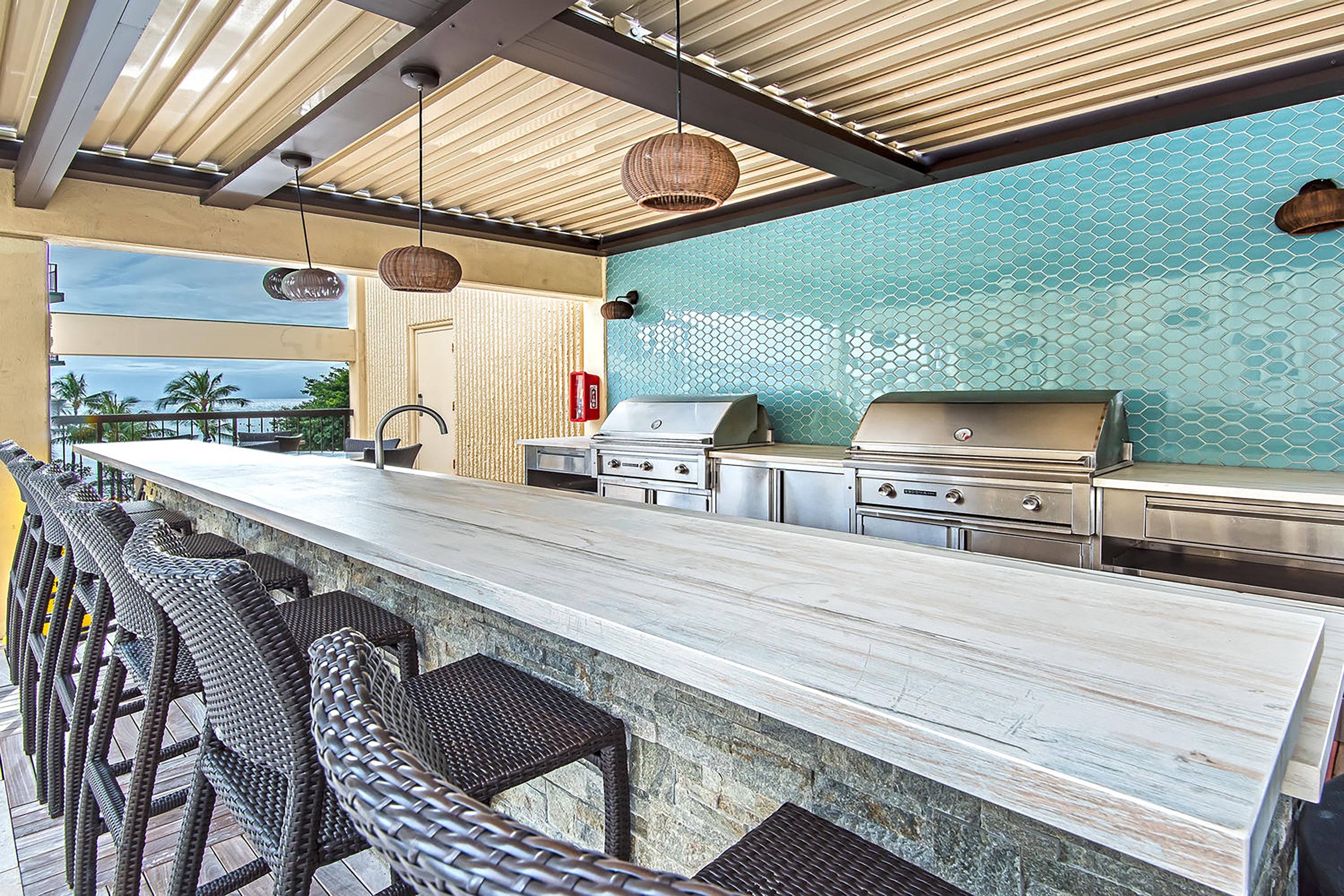 Een bar met een lange toonbank, rieten stoelen en een grillstation.