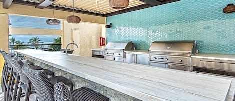 Een bar met een lange toonbank, rieten stoelen en een grillstation.