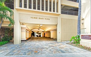 The entrance of Waikiki Beach Tower with a stone-tiled pathway leading to the entrance, palm trees, and a sign indicating the tower's name. - Ocean-beach Vacation Condo at Waikiki Beach Tower W/amazing Hotel Amenities (Honolulu)