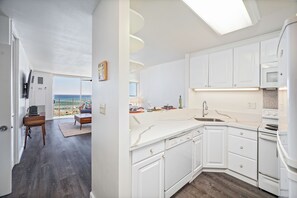 A modern kitchen with white cabinetry, a built-in oven, and a large window overlooking the sea. - Ocean-marina Views at Ilikai Marina W/full Kitchen Short Walk to the Beach (Honolulu)
