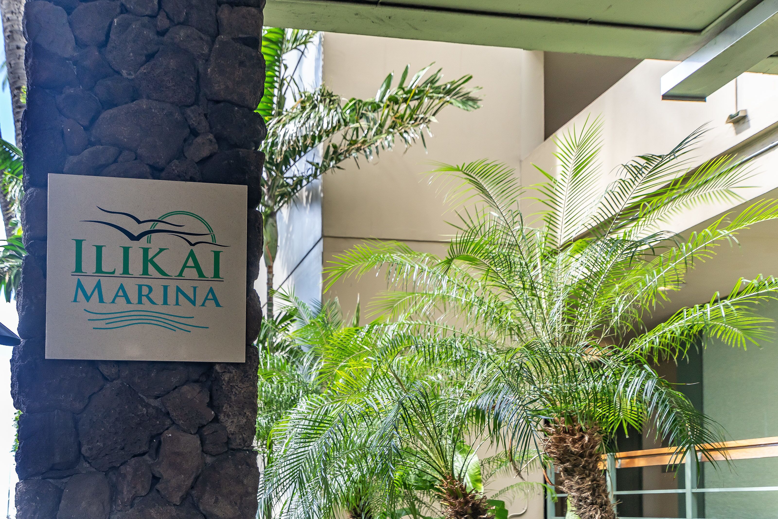 A sign for Ilikai Marina with a stone pillar and palm trees in the background.