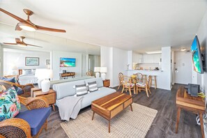 A modern living room with a sofa, chairs, a coffee table, and a dining area with chairs and a table. There is a kitchen area with cabinets and a television. - Ocean-marina Views at Ilikai Marina W/full Kitchen Short Walk to the Beach (Honolulu)