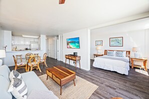 Een moderne, open woonruimte met een eethoek, een slaapkamer met een groot bed en nachtkastjes, en een keuken.