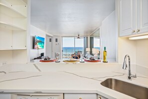 Een keuken met een groot raam, een roestvrijstalen spoelbak en uitzicht op de oceaan.