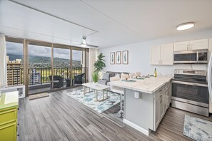 Eine moderne Küche mit einer großen Kochinsel, Edelstahlgeräten und Blick auf eine Stadtlandschaft durch große Fenster.