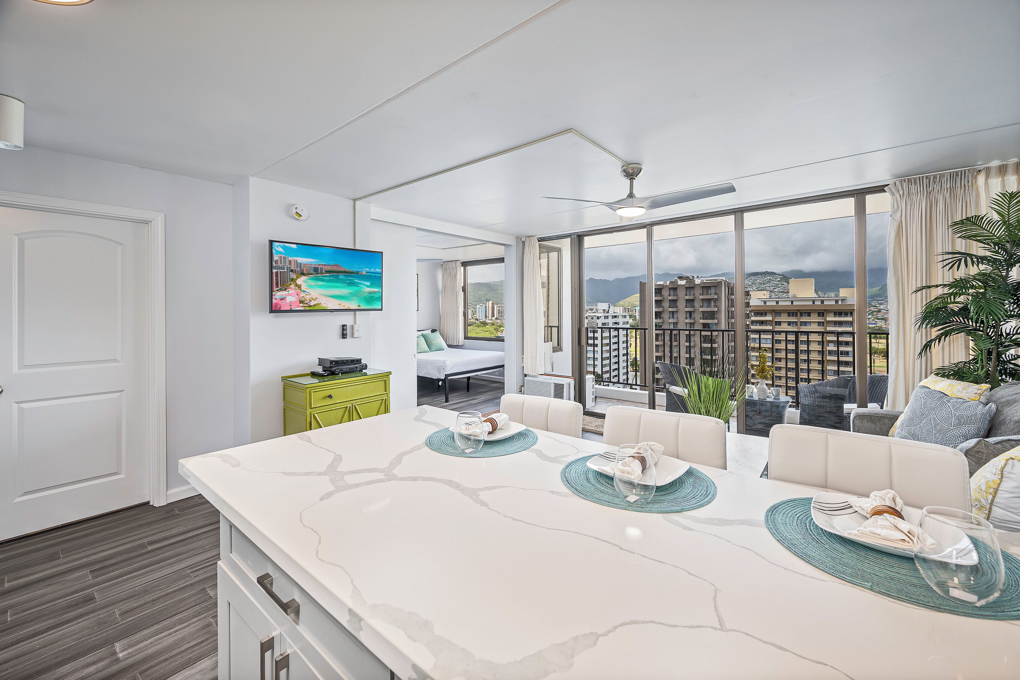 A modern hotel room with a large dining table, a bed, and a balcony with a city view.