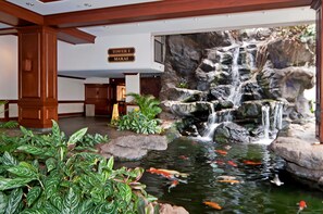 Un vestíbul d'hotel amb un estany de carps koi, una cascada i un senyal que indica 'Tower 1 Makai'.