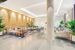 Eine großzügige Lobby mit modernem Design, inklusive einer großen Säule in der Mitte, Sofas, einem Couchtisch und Topfpflanzen.