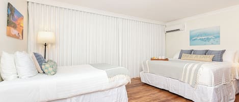 Habitación de hotel con dos camas, un ventanal con persianas, aire acondicionado de pared y un cuadro.