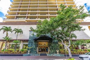 Un hôtel à plusieurs étages, doté d’une entrée imposante, de palmiers et d’un jardin bien entretenu.
