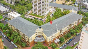A multi-story hotel with a central courtyard, surrounded by greenery and other buildings. - Modern Waikiki 1BR Condo at The Cove w/ Parking/prime Location Near Beach (Honolulu)