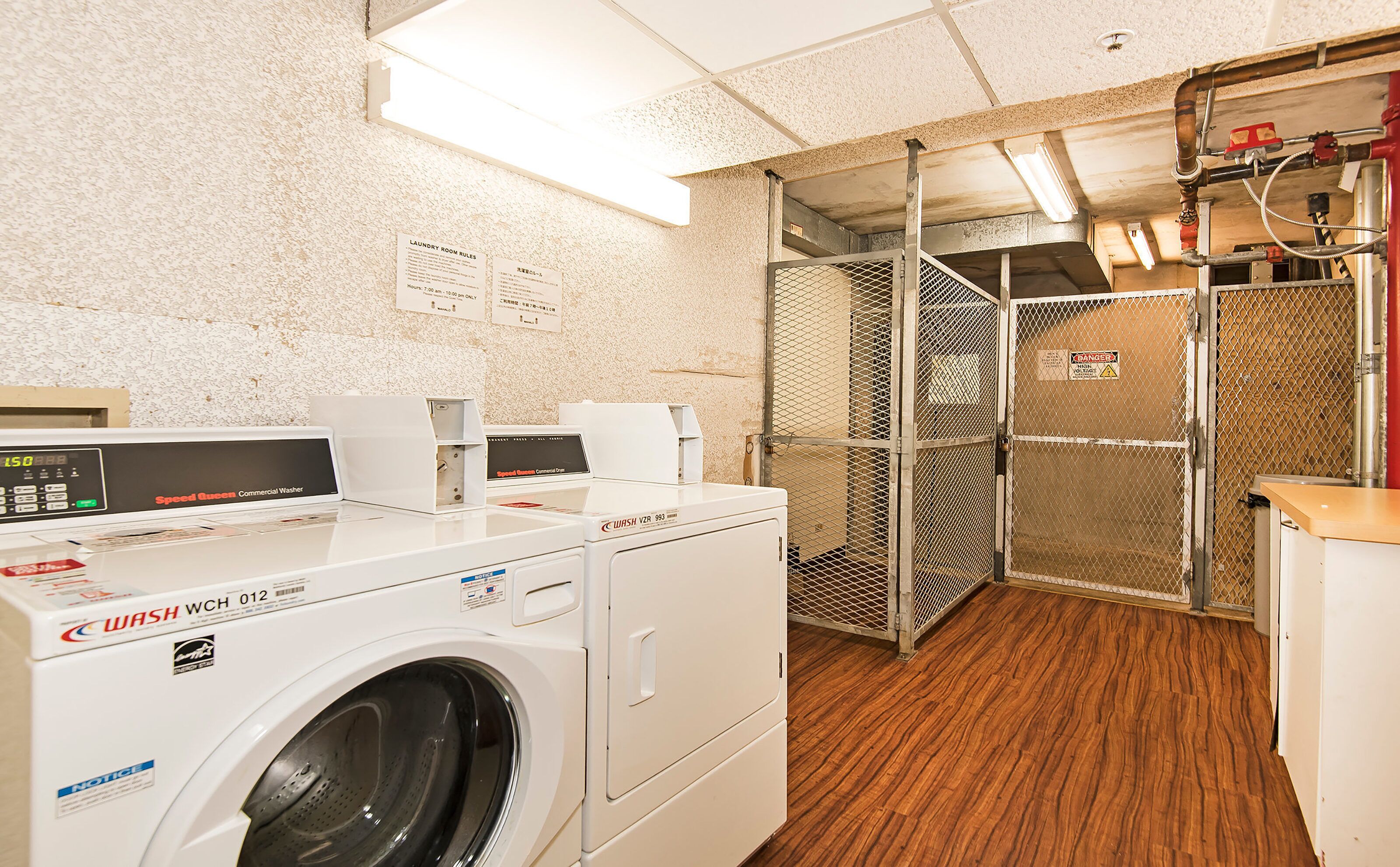 A commercial laundry facility with a front-loading washing machine, a dryer, and a metal mesh partition.