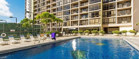 A hotel with a swimming pool, multiple balconies, and outdoor seating areas.