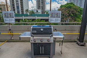 A portable barbecue grill with instructions, set against a chain-link fence with a cityscape in the background. - Golf Course-mountain Views Condo at Waikiki Sunset Half a Block to the Beach (Honolulu)