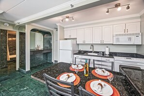 A modern kitchen with white cabinets, a black granite countertop, and a dining area with a table set for four. - Golf Course-mountain Views Condo at Waikiki Sunset Half a Block to the Beach (Honolulu)