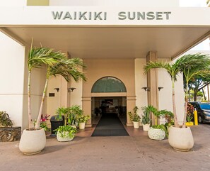 The entrance to Waikiki Sunset with a covered walkway, potted plants, and a clear view into the building. - Golf Course-mountain Views Condo at Waikiki Sunset Half a Block to the Beach (Honolulu)