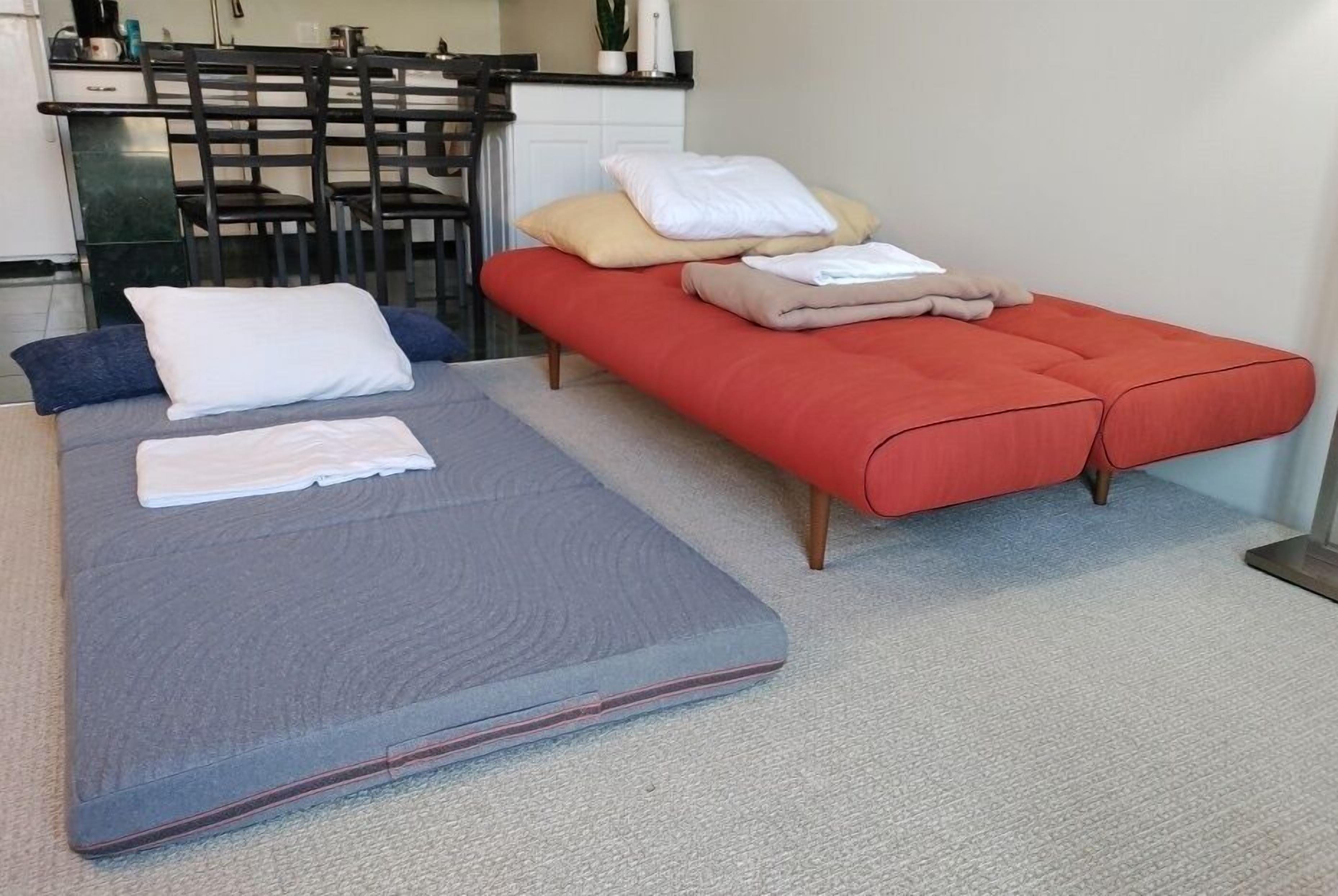A room with a bed, a bench, and a kitchenette area.