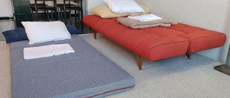 A room with a bed, a bench, and a kitchenette area.