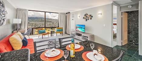 A modern hotel room with a dining area, a TV, and a view of the city.