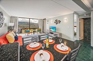 A modern hotel room with a dining area, a TV, and a view of the city. - Golf Course-mountain Views Condo at Waikiki Sunset Half a Block to the Beach (Honolulu)