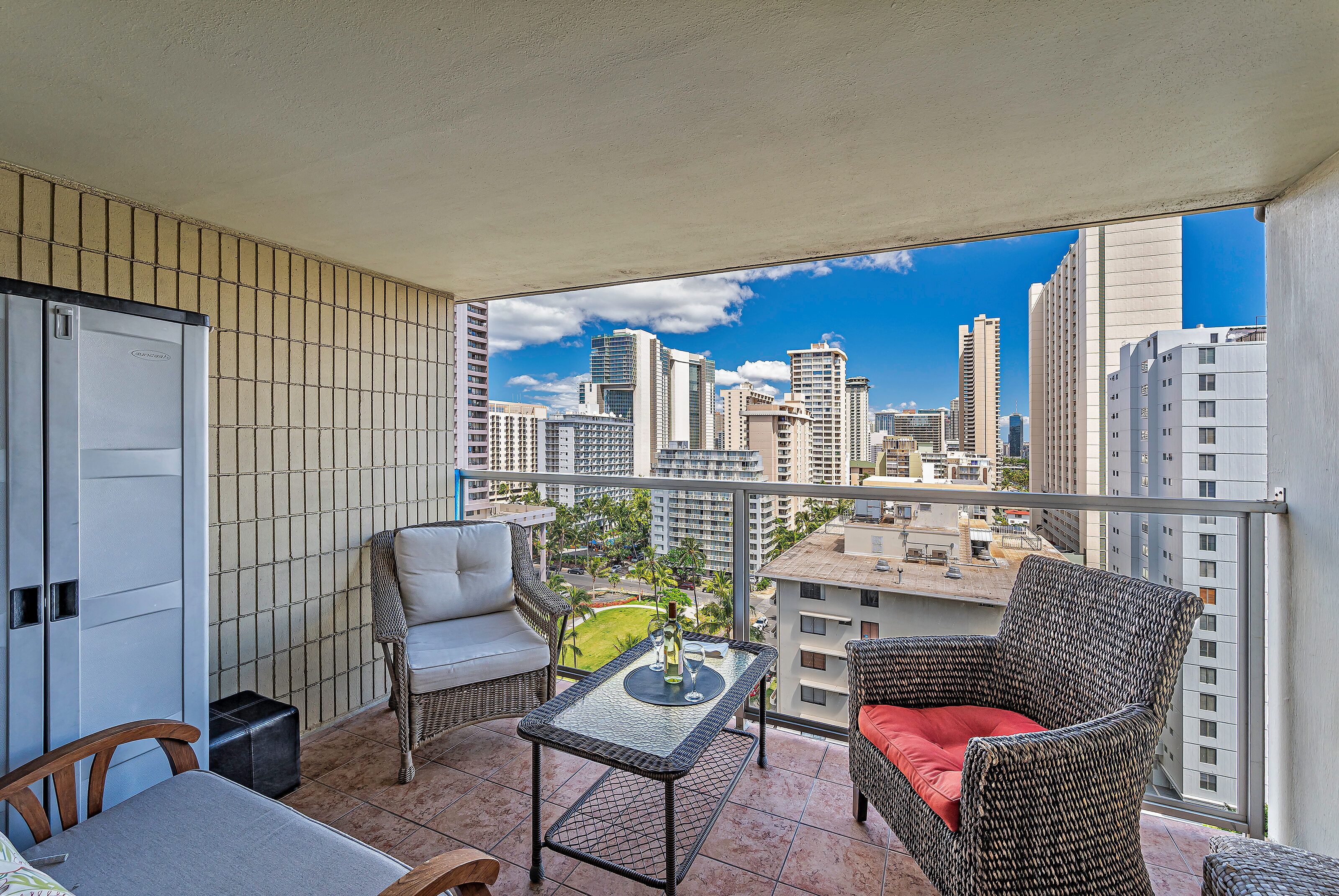 A balcony with wicker furniture, a table, and a view of a cityscape.