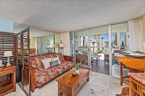 A spacious living area with a sofa, coffee table, and a view of the city through large windows. - Island Colony City-mountains View Condo Near Beach and Restaurants-shops (Honolulu)