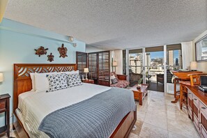 A hotel room with a large bed, a desk, a chair, and a view of the city through the balcony doors. - Island Colony City-mountains View Condo Near Beach and Restaurants-shops (Honolulu)