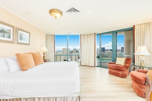 Ein Hotelzimmer mit einem großen Bett, einem roten Sessel, einem Glastisch und Blick auf die Stadt.