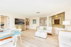 Ein modernes Wohnzimmer mit einem Glastisch, weißen Sofas und einem Gemälde, das eine Strandansicht zeigt.