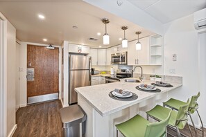 A modern kitchen with stainless steel appliances, a marble countertop, and green bar stools. - Ilikai Hotel Renovated Condo Steps Away From Beach W/free Wifi & Full Kitchen (Honolulu)