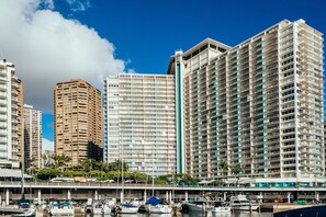 Hotel alto com várias varandas, um calçadão com barcos e um céu azul e límpido.