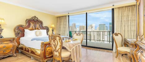 A spacious hotel room with a large bed, a dining area, and a balcony with a city view.