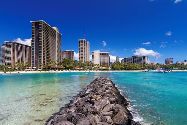 A coastal cityscape with high-rise buildings, a clear blue sky, and a rocky shoreline. - Royal Garden Couple's Getaway City-mt Views Condo W/kitchen & Near the Beach (Honolulu)