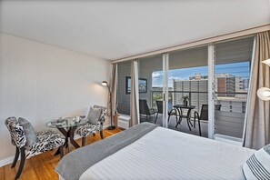 Ein Hotelzimmer mit einem großen Bett, einem kleinen Tisch, zwei Stühlen und einem Balkon mit Blick auf die Stadt.