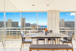 A dining area with a table set for four, large windows offering a city view, and a balcony with a railing. - Ocean-diamond Head Views PH Condo at Ilikai Hotel by the Beach W/full Kitchen (Honolulu)