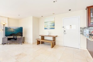 A modern living room with a flat-screen TV, a wooden bench, a painting, and a tiled floor. - Ocean-diamond Head Views PH Condo at Ilikai Hotel by the Beach W/full Kitchen (Honolulu)