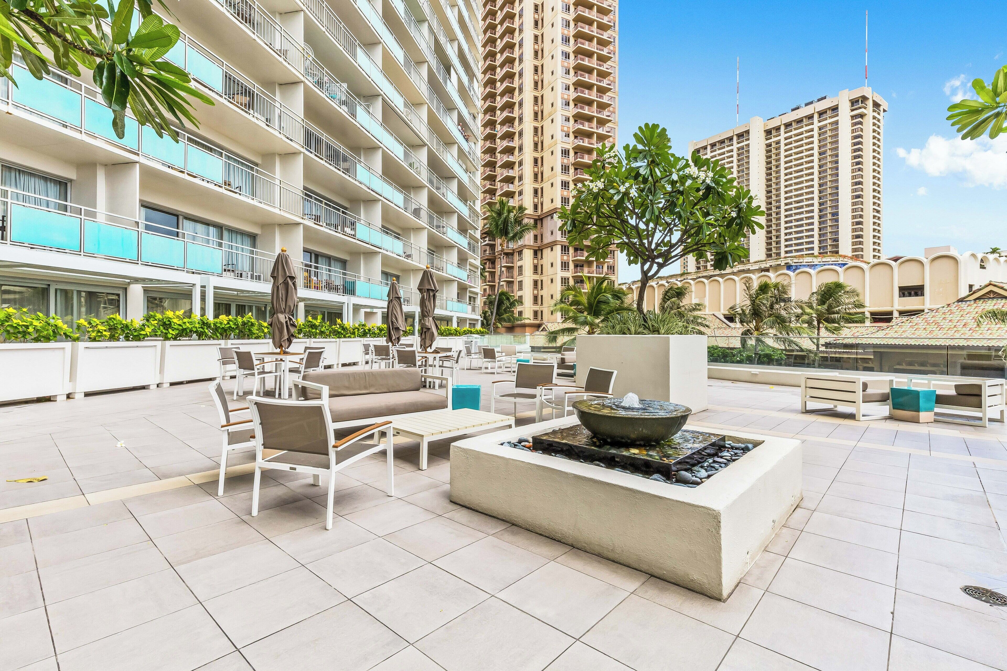 A rooftop terrace with outdoor seating, a fire feature, and a view of high-rise buildings.