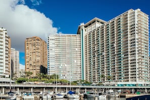 Un hôtel de grande hauteur doté de nombreux balcons, une marina avec des bateaux et un ciel d’un bleu éclatant.