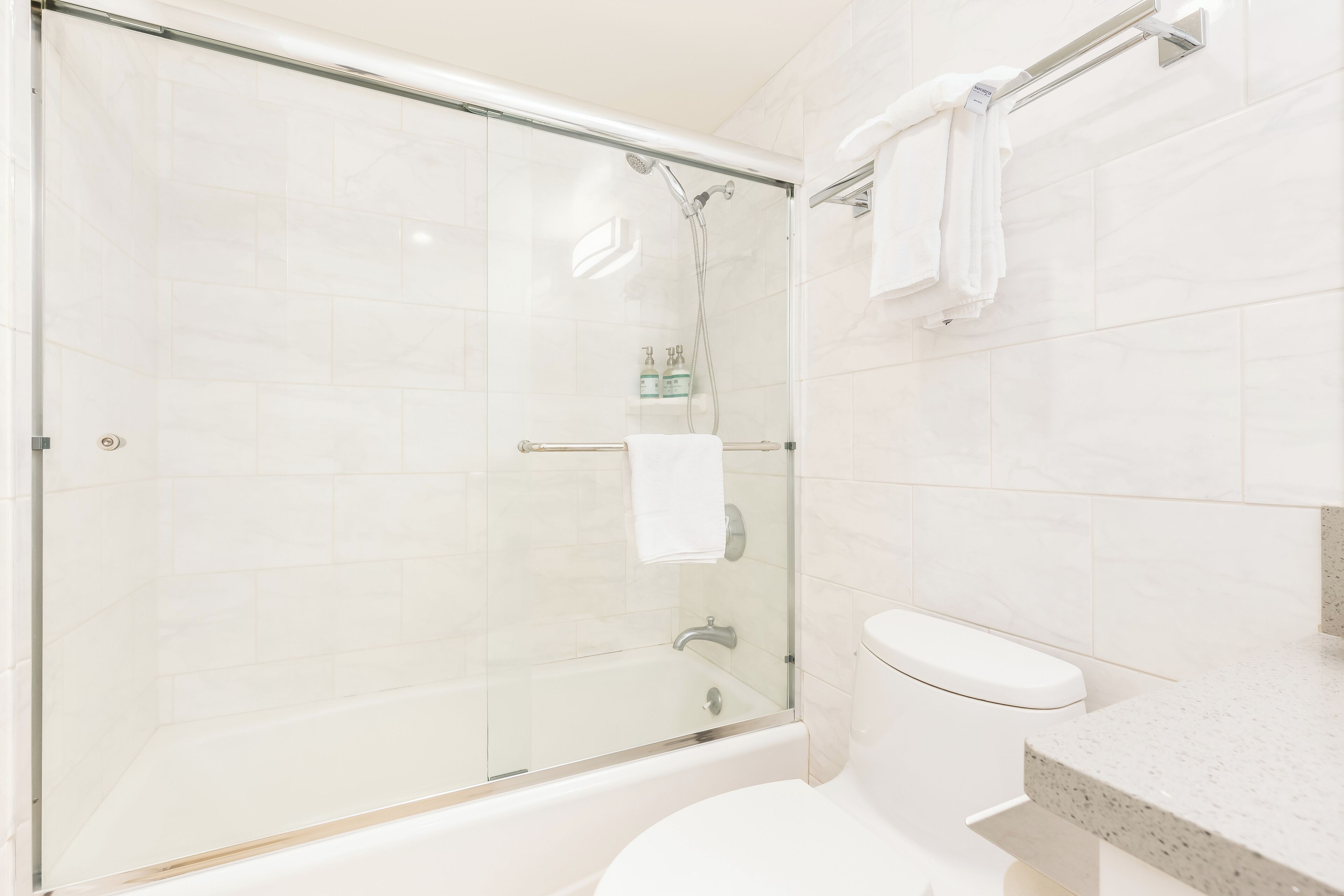 Ein modernes Badezimmer mit einer gläsernen Dusche, einer weißen Toilette und einem Waschtisch mit Handtuchhalter.