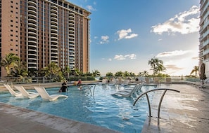 A swimming pool area with lounge chairs and a tall building in the background. - Ocean-diamond Head Views PH Condo at Ilikai Hotel by the Beach W/full Kitchen (Honolulu)