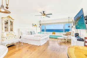 A room with a bed, seating area, and a large window with a view of the ocean. - Oceanfront W/sunset Views Condo at the Colony Surf Full Kitchen and Parking (Honolulu)