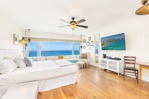 A bedroom with a large bed, a ceiling fan, a view of the ocean, a desk with a chair, and a television. - Oceanfront W/sunset Views Condo at the Colony Surf Full Kitchen and Parking (Honolulu)