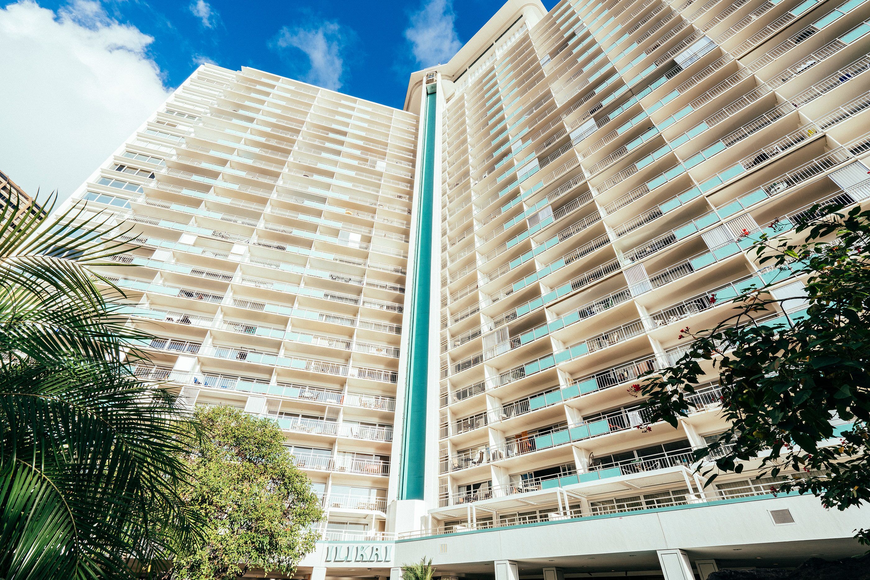 Un hotel de gran altura con varios balcones, una estructura vertical central y follaje circundante.