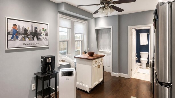 Una cucina moderna con una ventola a soffitto, una macchina da caffè, un frigorifero bianco e un'area pranzo con un tavolo in legno.