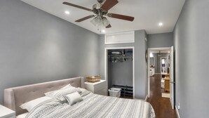 Una camera da letto con un letto, comodini, una ventola a soffitto, un armadio a muro e un bagno visibile attraverso una porta aperta.